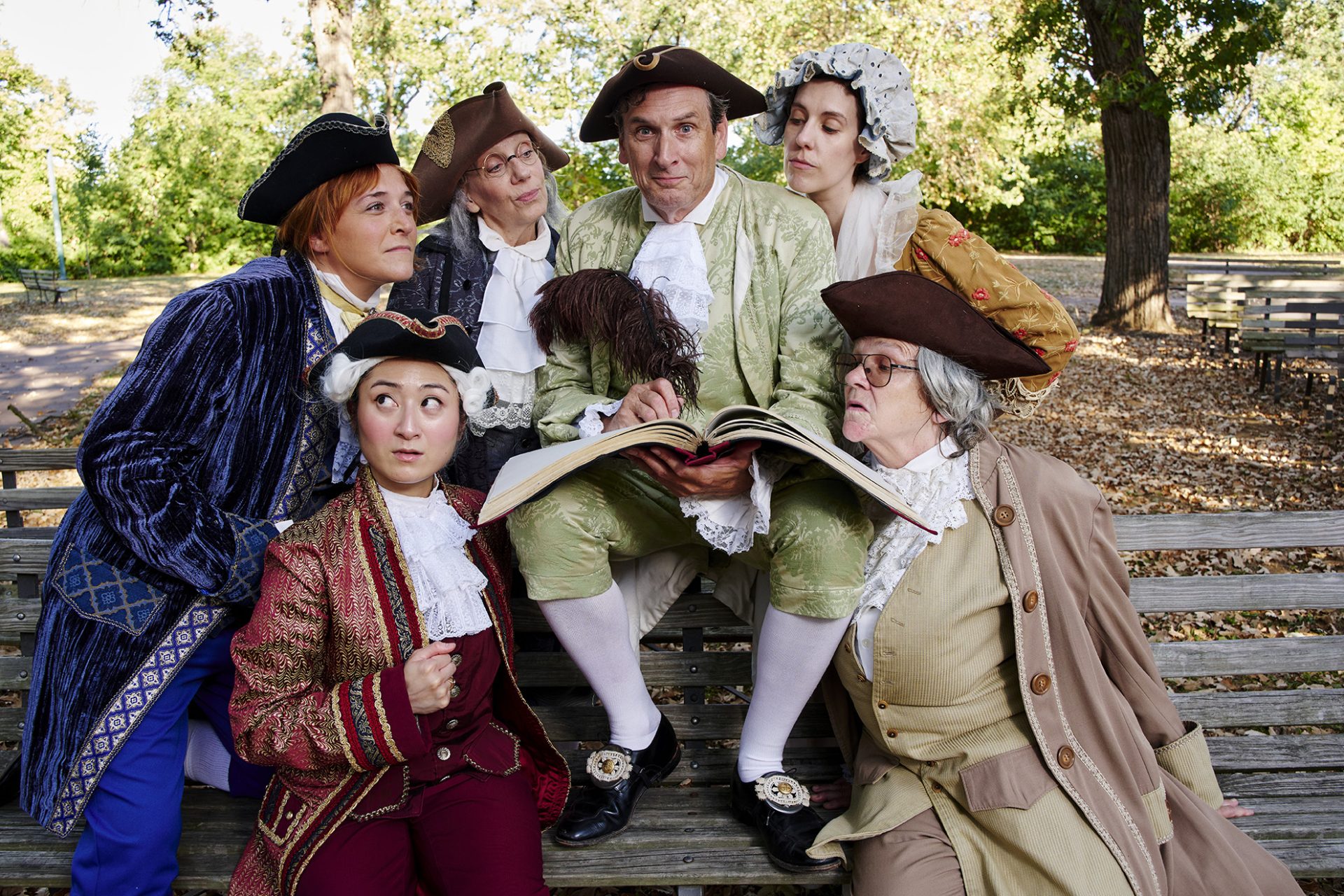 MORTON cast clustered on a park bench with a large open book